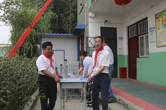 集團公司領(lǐng)導與學生一起將桌椅搬進教室